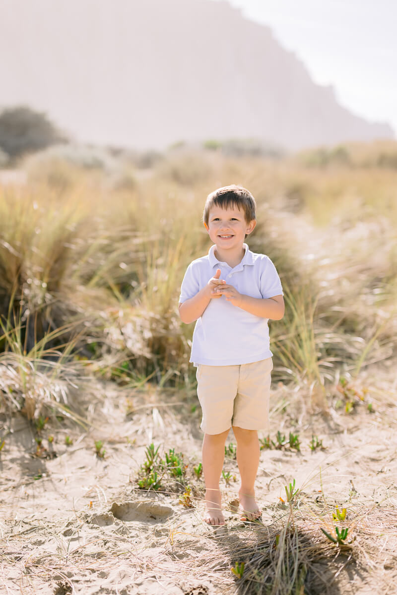 little boy in a light colored polo and khaki shorts on the beach after visiting San Luis Obispo Pediatricians