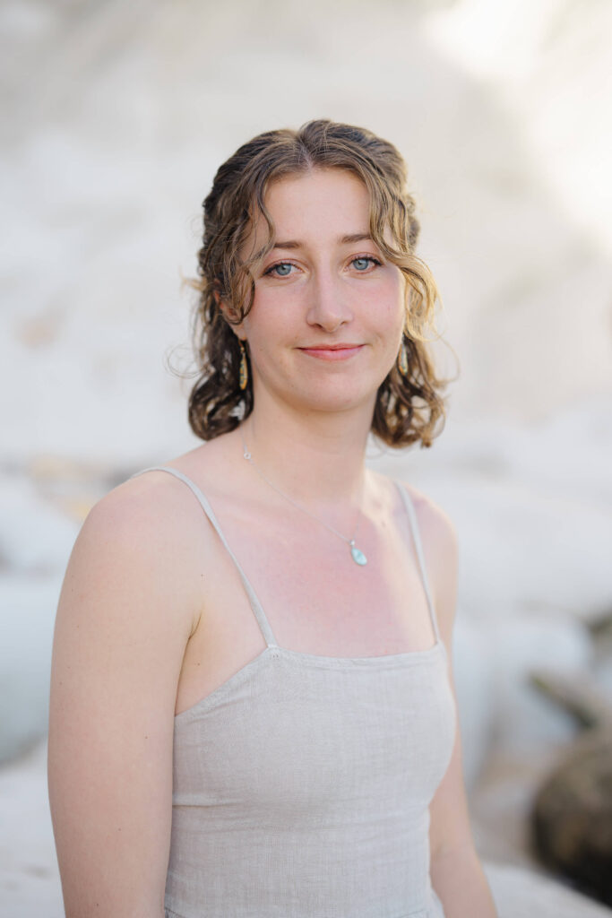 College senior from Cal Poly wearing a green graduation sash and neutral dress at Pismo Beach during her spring graduate portrait session with Rosa Clark Photography.